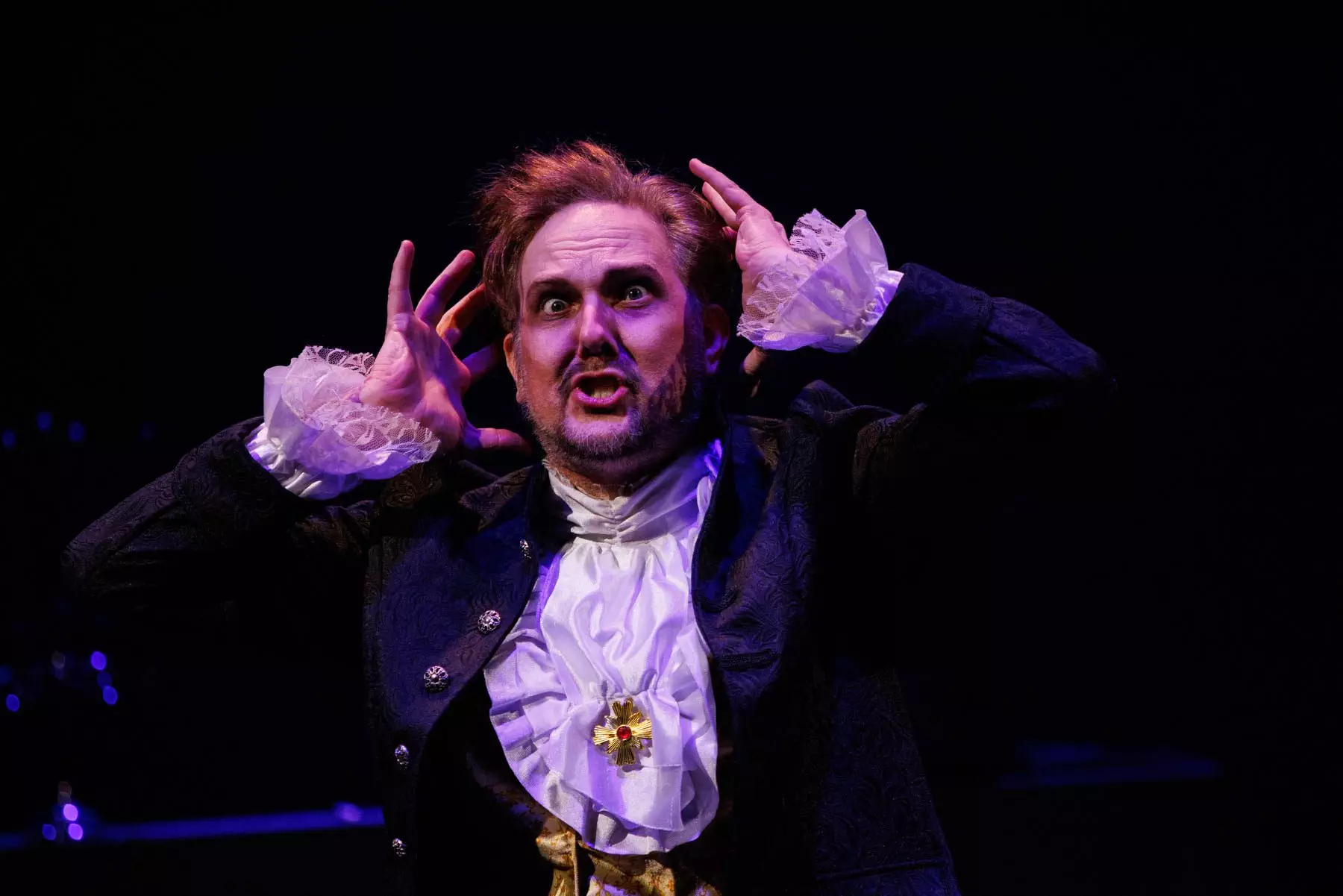 Kyle Hancock, as Sir Roderic Murgatroyd, performs "When the night wind howls" from Gilbert & Sullivan's "Ruddigore". He wears a frilled shirt and a dark jacket, and holds up his hands to his head with a crazed expression.